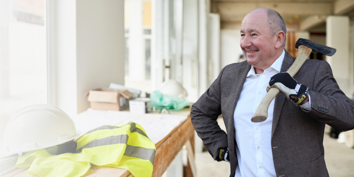 Bild von Dr. Franz Metz im Anzug mit Werkzeug, im Hintergrund eine Baustelle